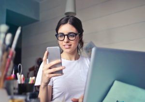 Person looking at their phone while sitting in front of a laptop